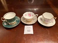 Front view of all 3 cups and saucers showing decorative floral and gold designs.