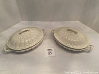 Two off-white ironstone tureens with lids side by side, showing overall shape and handles.