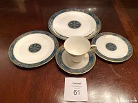 Five-piece place setting displayed on wooden table: dinner plate, salad plate, bread plate, cup and saucer