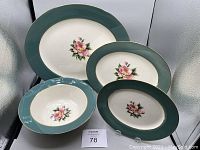 Four ceramic serving dishes of various sizes with a green rim and pink rose floral decoration in the center, displayed against a white background.