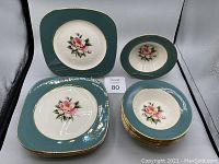 Set of 8 square bread plates and 8 round fruit bowls with teal borders and floral pattern.