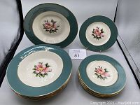 Set of 8 side plates and 8 soup bowls arranged in groups with visible floral design and teal border.