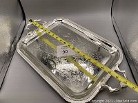 Top view showing the engraved decorative floral and scroll design on the metal tray surface with measuring tape across its length indicating about 20 inches.