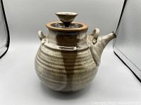 Front and side view of a vintage ceramic tea pot showing round ribbed body, two small handles, spout and lid with knob.