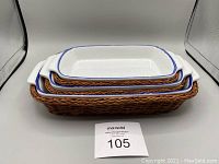 Three stackable white ceramic casseroles with blue rims placed in brown woven wicker baskets, shown stacked and unstacked to display all pieces.