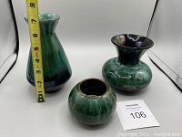 Three Blue Mountain Pottery ceramic pieces: one tall vase, one short vase, one bowl, all green and blue glazed, placed with measuring tape indicating approx. 7 inches for the tallest vase.