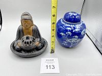 Two items side by side: Buddha incense holder and blue ginger jar with measuring tape showing height approximately 7 inches (18 cm)