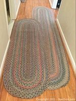 Photo showing two oval braided runners placed on wooden floor in hallway. The runners display a traditional braided pattern with mixed muted colors.