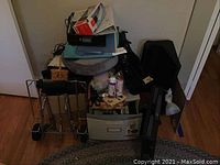 General photo showing the metal luggage cart, plastic rolling crate, briefcase, desk lamp, lap desks, and miscellaneous office supplies stacked together.