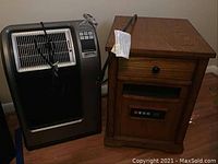 Photo showing Lasko heater and Twin Star wooden heater side by side on floor.
