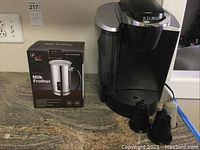 Keurig coffee maker with two coffee pods and Chef's Star Milk Frother box side by side on counter.