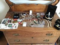 Wide view of all jewelry pieces spread across wooden furniture including watches in boxes, chains, brooches, and other assorted items.
