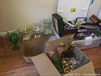 Various glass vases and Longaberger basket with handle seen on floor next to a plastic bin with miscellaneous items inside, including candle holders and figurines.