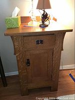 Front view of vintage wood nightstand with drawer and cabinet door, wood grain and metal hardware visible.