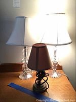 Three lamps on wooden surface: two glass lamps behind, one brown-shade lamp front