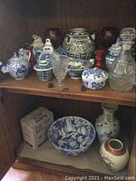Shelf with blue and white porcelain teapots, bowls and jars, glass decanter, glass and porcelain pitchers