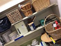 Photo showing four assorted woven baskets and a white small table with boxes and items around and on the shelf.