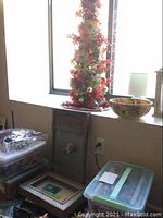 Photo of decorated tabletop Christmas tree near window along with plastic storage bins and vintage washboard leaning against wall.