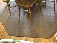 Photo of octagonal brown rug under wooden dining table and chairs with visible texture and wear.