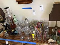 Table setup with various Looney Tunes Pepsi collectible glasses including Tweety Bird, shot glasses, wine glasses, cocktail shaker, and two brown lamps with fabric shades.