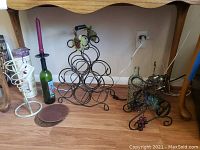 Photo showing metal wire wine racks, candle holder bottle with purple candle, wooden boxes, and decorative bottle lantern and cork holder on floor.