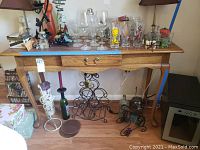 Full front view of the wooden sofa table with a drawer, showing table top with various household items and underneath wine racks.