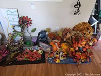 Wide view showing a variety of fall decorations including pumpkin figurines, fall leaves, wreaths, string lights, wood signs, and metal ornaments arranged on the floor near a wall.