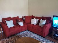 Red fabric sectional sofa positioned in corner area, showing multiple cushions and pillows.