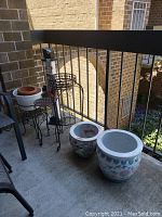 Photo of the balcony showing five metal plant stands, two ceramic planters, and the snowman stand with overall weathered condition