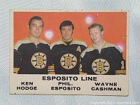 Front of the hockey card showing color photo of Ken Hodge, Phil Esposito, and Wayne Cashman in Boston Bruins jerseys with text naming players and team line