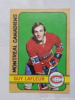 Front image showing Montreal Canadiens Guy Lafleur in his red uniform from 1972 O-Pee-Chee card with green background and beige borders.