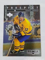 Front of the 1998 Upper Deck Black Diamond Daniel Sedin rookie card showing player skating in yellow Sweden uniform with helmet blue and number 12.