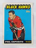 Front view of Phil Esposito rookie hockey card with Chicago Black Hawks uniform, Topps brand, blue background, and Black Hawks title at top.