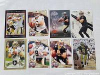 Photo of eight Drew Brees football trading cards laid out on a white surface, each showing Brees in New Orleans Saints uniform, in action or ready pose.