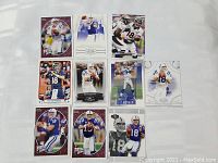 Top-down view of 10 Peyton Manning football trading cards arranged on white surface, showing various player poses and team uniforms