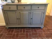 Front view of gray painted wooden console cabinet with three drawers above and four doors below.