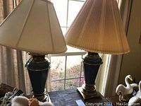 Pair of two decorative Stiffel lamps with tapered bases and pleated lamp shades shown on a wooden table near window.