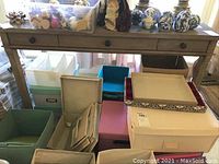 Front view of wooden Pottery Barn writing desk with three drawers, surrounded by storage boxes and various items on top of the desk.