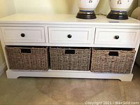 Front view of white storage unit showing three drawers on top and three wicker bins below