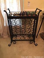 Full front view showing the black metal wine rack holding wine bottles and the removable top tray.