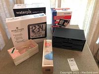 Collection of all items including boxed water flosser, boxed atomic clock, boxed blood pressure monitor, stationery organizer, stationery set, and ice bag box on table