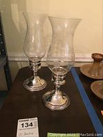Pair of clear glass hurricane lamps with sterling silver bases on a table.