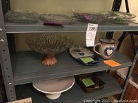 Three shelves of vintage serving platters and other items including the ceramic pitcher and brass basket, showing the overall contents of the lot.