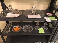 Full view of lot on shelf showing multiple glass serving dishes and two crystal candlesticks.