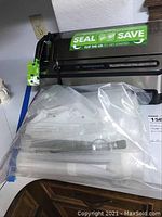 Clear plastic bag containing vacuum sealer accessories including extra rolls and attachments, placed in front of closed FoodSaver vacuum sealer machine