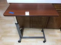 Front view of adjustable rolling bed tray showing wood finish top and metal frame base with wheels.