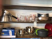 Shelf with Pyrex measuring cups of different sizes, metal strainers including large colander, and glass bowls.
