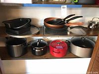 Overview of various kitchenware items including Staub Dutch oven, skillets, saucepans, stock pots, and baking pans arranged on shelves.