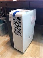 Angled front view of the white and black Danby dehumidifier on wood floor