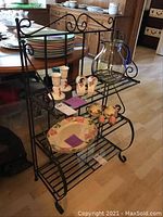 Full view of the black wrought iron shelving unit with multiple decorative items placed on the shelves, shown in a room with wood flooring.